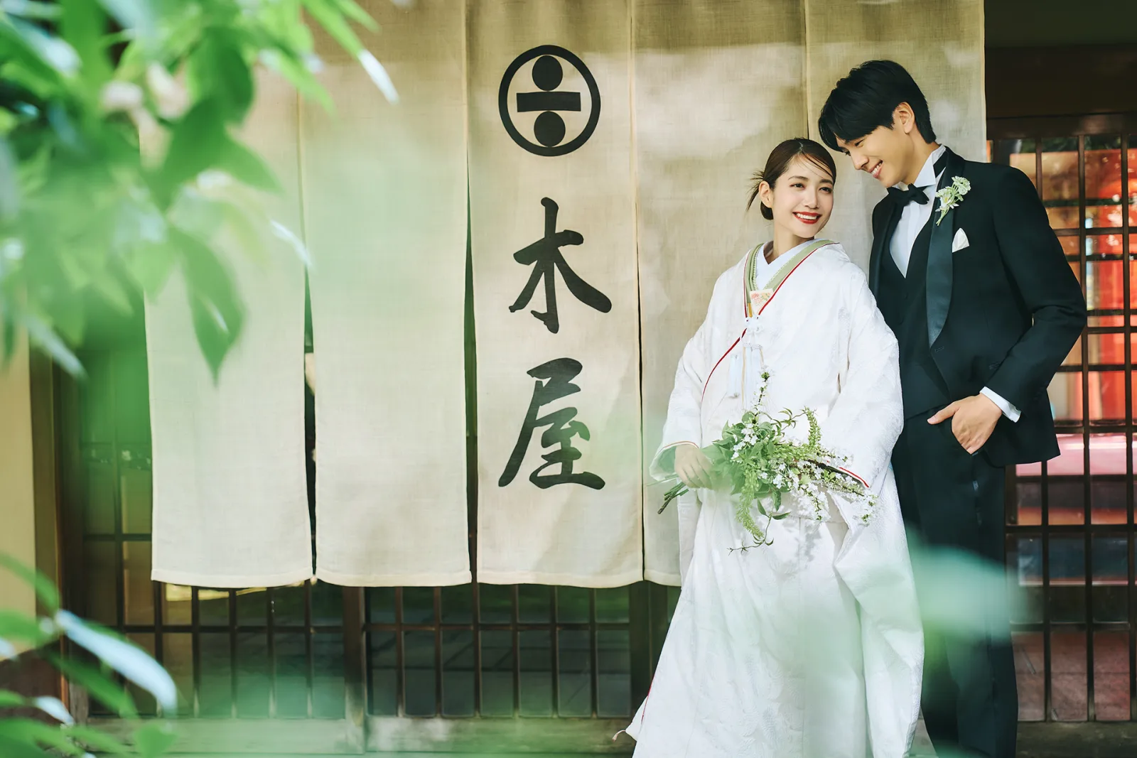 Couple at the Bettei Kiya entrance, beneath the noren curtain carrying the Kiya crest